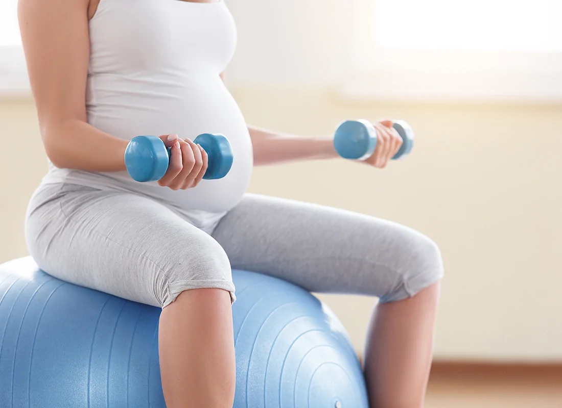 pregnant woman exercising with hand weights on a pilates ball